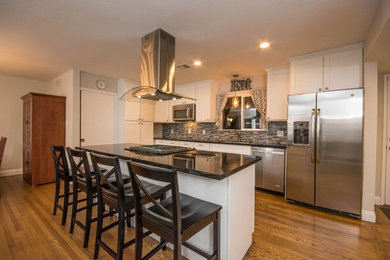 Example of a large transitional l-shaped medium tone wood floor and brown floor eat-in kitchen design in Sacramento with a single-bowl sink, shaker cabinets, white cabinets, solid surface countertops, multicolored backsplash, ceramic backsplash, stainless steel appliances and an island