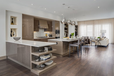 This is an example of an expansive contemporary l-shaped kitchen/diner in Calgary with a submerged sink, flat-panel cabinets, engineered stone countertops, medium hardwood flooring, an island, medium wood cabinets, white splashback, stone tiled splashback and integrated appliances.