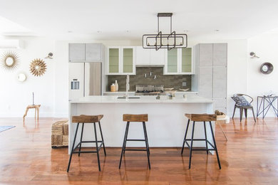 Inspiration for a mid-sized contemporary galley medium tone wood floor and brown floor open concept kitchen remodel in New York with an undermount sink, flat-panel cabinets, white cabinets, quartz countertops, gray backsplash, glass tile backsplash, stainless steel appliances and an island