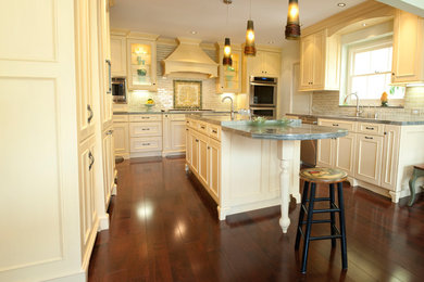 Mid-sized elegant u-shaped medium tone wood floor and brown floor eat-in kitchen photo in Los Angeles with yellow cabinets, granite countertops, green backsplash, ceramic backsplash, stainless steel appliances, an island, an undermount sink and beaded inset cabinets