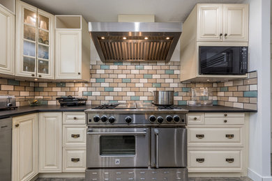 Eat-in kitchen - mid-sized traditional l-shaped gray floor eat-in kitchen idea in Vancouver with an undermount sink, raised-panel cabinets, multicolored backsplash, ceramic backsplash, stainless steel appliances and an island