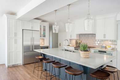 Example of a large beach style medium tone wood floor and brown floor kitchen design in Vancouver with recessed-panel cabinets, white cabinets, quartz countertops, gray backsplash, stainless steel appliances, an island, gray countertops, a double-bowl sink and subway tile backsplash