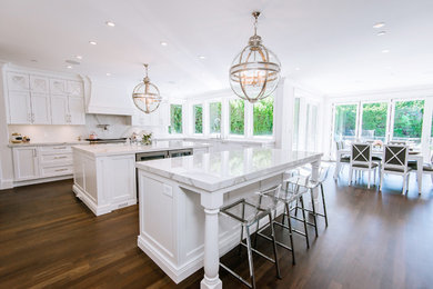 Open concept kitchen - large contemporary u-shaped medium tone wood floor open concept kitchen idea in Vancouver with a farmhouse sink, recessed-panel cabinets, white cabinets, quartz countertops, white backsplash, stone slab backsplash, stainless steel appliances and two islands