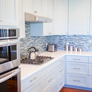 This is an example of a mid-sized beach style l-shaped eat-in kitchen in Atlanta with an undermount sink, louvered cabinets, blue cabinets, blue splashback, glass tile splashback, stainless steel appliances, medium hardwood floors and with island.