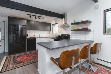 Inredning av ett modernt mellanstort grå grått kök, med en nedsänkt diskho, släta luckor, vita skåp, bänkskiva i kalksten, vitt stänkskydd, stänkskydd i tunnelbanekakel, svarta vitvaror, ljust trägolv, en halv köksö och grått golv