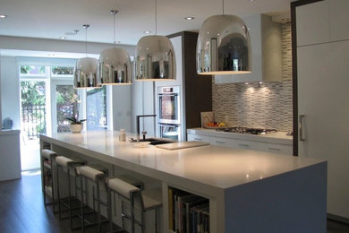 Photo of a medium sized contemporary galley kitchen/diner in Calgary with a double-bowl sink, flat-panel cabinets, white cabinets, composite countertops, beige splashback, matchstick tiled splashback, integrated appliances, dark hardwood flooring, an island and brown floors.