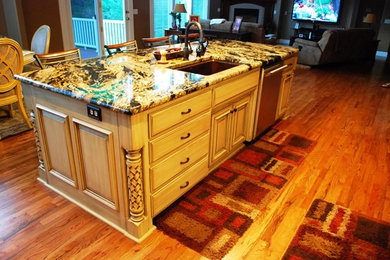 Example of a mid-sized classic u-shaped medium tone wood floor and brown floor enclosed kitchen design in Kansas City with an undermount sink, raised-panel cabinets, beige cabinets, stainless steel appliances and an island