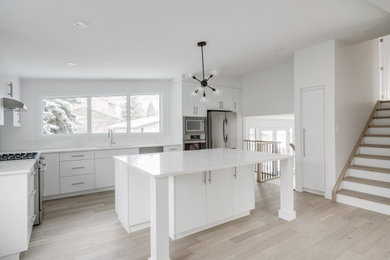 Eat-in kitchen - mid-sized transitional u-shaped light wood floor and beige floor eat-in kitchen idea in Calgary with an undermount sink, flat-panel cabinets, white cabinets, quartzite countertops, white backsplash, stone slab backsplash, stainless steel appliances, an island and white countertops