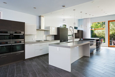 Inspiration for a contemporary galley open plan kitchen in Calgary with a built-in sink, flat-panel cabinets, white cabinets, engineered stone countertops, white splashback, metro tiled splashback and integrated appliances.