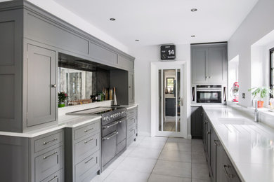 This is an example of a large traditional galley enclosed kitchen in Kent with a submerged sink, shaker cabinets, grey cabinets, black splashback, glass sheet splashback, integrated appliances, no island, grey floors and white worktops.