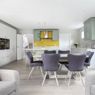 Design ideas for a contemporary u-shaped open plan kitchen in Buckinghamshire with shaker cabinets, green cabinets, yellow splashback, glass sheet splashback, stainless steel appliances, with island, grey floor and white benchtop.