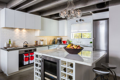 ロサンゼルスにあるコンテンポラリースタイルのおしゃれなL型キッチン (フラットパネル扉のキャビネット、白いキャビネット、白いキッチンパネル、サブウェイタイルのキッチンパネル、シルバーの調理設備) の写真