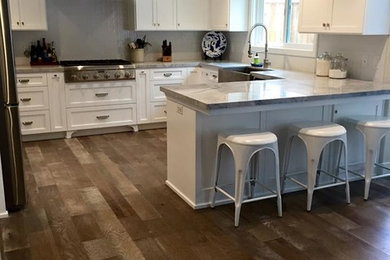 Example of a mid-sized beach style u-shaped kitchen design in San Luis Obispo with a farmhouse sink, shaker cabinets, white cabinets, quartzite countertops, white backsplash and stainless steel appliances
