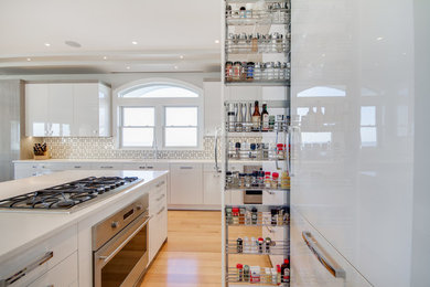 This is an example of a large contemporary l-shaped open plan kitchen in Philadelphia with flat-panel cabinets, white cabinets, light hardwood flooring, a submerged sink, white splashback, ceramic splashback, an island, stainless steel appliances, quartz worktops and brown floors.