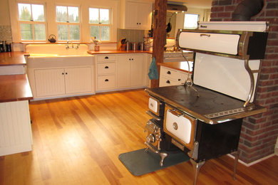 Modelo de cocina de estilo de casa de campo con fregadero sobremueble, puertas de armario blancas, encimera de madera y armarios con rebordes decorativos