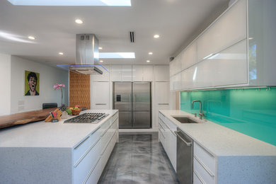 Example of a mid-sized minimalist l-shaped concrete floor eat-in kitchen design with a drop-in sink, stainless steel appliances, an island, flat-panel cabinets, white cabinets, quartzite countertops, green backsplash and glass sheet backsplash