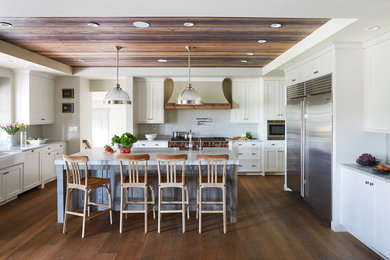 Inspiration for a mid-sized timeless u-shaped dark wood floor and brown floor kitchen remodel in Chicago with a farmhouse sink, shaker cabinets, white cabinets, white backsplash, stainless steel appliances, an island, gray countertops, marble countertops and subway tile backsplash
