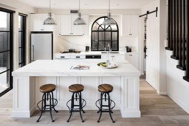 Inspiration for a large urban galley open plan kitchen in Melbourne with a double-bowl sink, recessed-panel cabinets, white cabinets, engineered stone countertops, white splashback, marble splashback, white appliances, medium hardwood flooring, an island and grey floors.