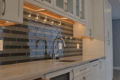 Example of a large mid-century modern single-wall open concept kitchen design in Philadelphia with a farmhouse sink, shaker cabinets, white cabinets, gray backsplash, stainless steel appliances and an island