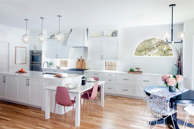Eat-in kitchen - large transitional l-shaped light wood floor and brown floor eat-in kitchen idea in Austin with a single-bowl sink, shaker cabinets, white cabinets, quartz countertops, white backsplash, ceramic backsplash, stainless steel appliances, an island and white countertops