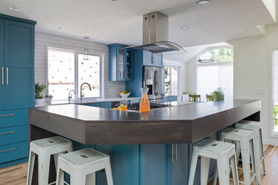 Example of a mid-sized trendy medium tone wood floor and brown floor eat-in kitchen design in Other with a single-bowl sink, shaker cabinets, blue cabinets, quartz countertops, white backsplash, subway tile backsplash, stainless steel appliances, an island and white countertops