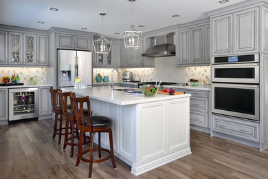Design ideas for a large traditional l-shaped kitchen/diner in Other with a double-bowl sink, raised-panel cabinets, grey cabinets, engineered stone countertops, white splashback, porcelain splashback, stainless steel appliances, medium hardwood flooring, an island and beige floors.