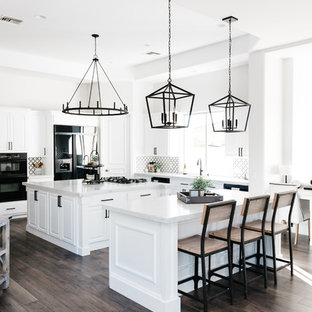 Immagine di una cucina tradizionale con lavello sottopiano, ante bianche, top in quarzo composito, paraspruzzi nero, paraspruzzi in marmo, elettrodomestici neri, pavimento in legno massello medio, 2 o più isole, pavimento marrone e top bianco