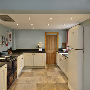 This is an example of a large victorian l-shaped separate kitchen in Other with a farmhouse sink, beaded inset cabinets, beige cabinets, black splashback, slate splashback, coloured appliances, slate floors and beige floor.