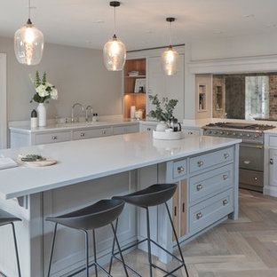 Design ideas for a classic kitchen in Hertfordshire with shaker cabinets, grey cabinets, mirror splashback, stainless steel appliances, light hardwood flooring, an island, brown floors and white worktops.