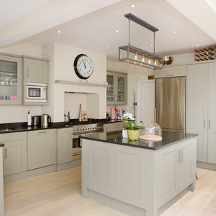 Design ideas for a traditional eat-in kitchen in London with a double-bowl sink, shaker cabinets, grey cabinets, stainless steel appliances, light hardwood floors, with island and granite benchtops.