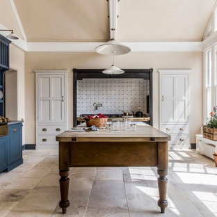 Foto di una grande cucina a L tradizionale chiusa con lavello stile country, ante con riquadro incassato, ante blu, paraspruzzi bianco, paraspruzzi in gres porcellanato, elettrodomestici da incasso, pavimento in pietra calcarea, isola, pavimento beige, top in legno e top marrone
