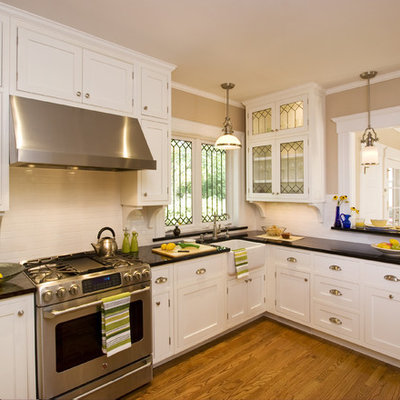 Enclosed kitchen - mid-sized traditional u-shaped medium tone wood floor enclosed kitchen idea in New York with beaded inset cabinets, paneled appliances, a farmhouse sink, granite countertops, white backsplash, ceramic backsplash, a peninsula and white cabinets