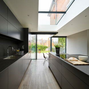 Esempio di una cucina minimalista con lavello a doppia vasca, ante lisce, ante nere, paraspruzzi nero, elettrodomestici da incasso, pavimento in legno massello medio, pavimento marrone e top nero