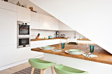 Large modern l-shaped kitchen in Other with flat-panel cabinets, white cabinets, wood worktops, white splashback, metro tiled splashback, stainless steel appliances, light hardwood flooring and an island.