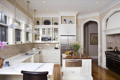 This is an example of a large traditional u-shaped enclosed kitchen in New York with glass-front cabinets, stainless steel appliances, marble worktops, a double-bowl sink, white cabinets, beige splashback, metro tiled splashback, medium hardwood flooring, an island, brown floors and grey worktops.
