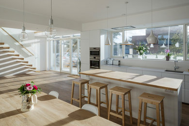 Foto de cocina lineal contemporánea de tamaño medio abierta con fregadero integrado, armarios con paneles lisos, puertas de armario blancas, encimera de madera, electrodomésticos con paneles y una isla