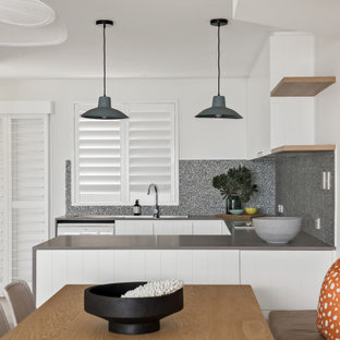 Design ideas for a contemporary u-shaped eat-in kitchen in Sunshine Coast with an integrated sink, flat-panel cabinets, white cabinets, grey splashback, stainless steel appliances, a peninsula and grey benchtop.