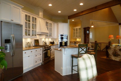 Diseño de cocina de estilo americano con fregadero sobremueble, armarios con paneles empotrados, puertas de armario blancas, encimera de granito, suelo de madera oscura y una isla