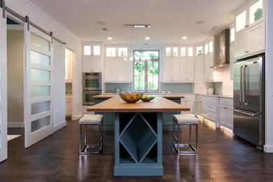 Example of a large trendy l-shaped dark wood floor open concept kitchen design in Dallas with a farmhouse sink, shaker cabinets, white cabinets, blue backsplash, glass tile backsplash, stainless steel appliances, two islands and wood countertops