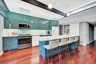 Mid-sized trendy galley medium tone wood floor and brown floor kitchen photo in Sacramento with quartz countertops, glass sheet backsplash, an undermount sink, flat-panel cabinets, green cabinets, green backsplash, white appliances and an island