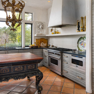 Modelo de cocina en U, ecléctica, de tamaño medio, con armarios con paneles lisos, puertas de armario grises, encimera de acrílico, salpicadero verde, salpicadero de azulejos tipo metro, electrodomésticos de acero inoxidable, suelo de baldosas de terracota, una isla y fregadero bajoencimera