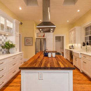 Inspiration for a large country galley kitchen pantry in Other with a belfast sink, shaker cabinets, white cabinets, wood worktops, white splashback, mosaic tiled splashback, stainless steel appliances, medium hardwood flooring, an island and orange floors.