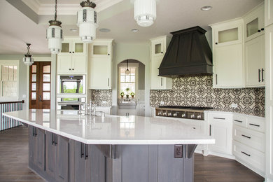Example of a large transitional l-shaped dark wood floor and brown floor open concept kitchen design in Minneapolis with a farmhouse sink, shaker cabinets, white cabinets, quartz countertops, multicolored backsplash, cement tile backsplash, paneled appliances and an island