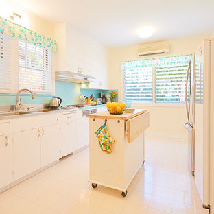 Design ideas for a large tropical galley separate kitchen in Hawaii with a double-bowl sink, flat-panel cabinets, white cabinets, laminate benchtops, blue splashback, stainless steel appliances, vinyl floors and with island.