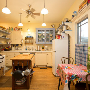 Inspiration for a small shabby-chic style l-shaped separate kitchen in Other with an undermount sink, shaker cabinets, white cabinets, tile benchtops, white splashback, timber splashback, white appliances, light hardwood floors, with island and brown floor.