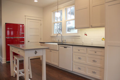 Example of a mid-sized classic galley medium tone wood floor enclosed kitchen design in Other with a farmhouse sink, shaker cabinets, white cabinets, solid surface countertops, white backsplash, mosaic tile backsplash, white appliances and an island