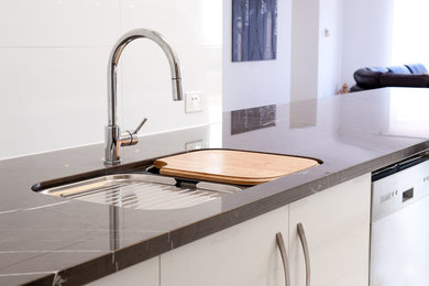 Modern inredning av ett mellanstort kök, med en undermonterad diskho, släta luckor, vita skåp, marmorbänkskiva, spegel som stänkskydd, rostfria vitvaror och en halv köksö