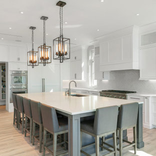 Foto di un'ampia cucina a L stile marino con lavello sottopiano, ante in stile shaker, ante bianche, paraspruzzi grigio, elettrodomestici in acciaio inossidabile, isola, pavimento beige e top beige