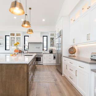 Inspiration for a transitional l-shaped medium tone wood floor and brown floor kitchen remodel in Orange County with an undermount sink, shaker cabinets, white cabinets, white backsplash, stainless steel appliances, an island and gray countertops