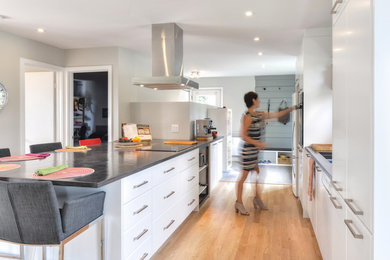 Photo of a medium sized modern open plan kitchen in Montreal with a submerged sink, flat-panel cabinets, white cabinets, concrete worktops, white splashback, metro tiled splashback, stainless steel appliances, light hardwood flooring and an island.